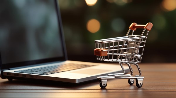 Webshop erstellen lassen Kleiner Einkaufswagen neben einem Laptop. Metapher für das Erstellen eines Webshops